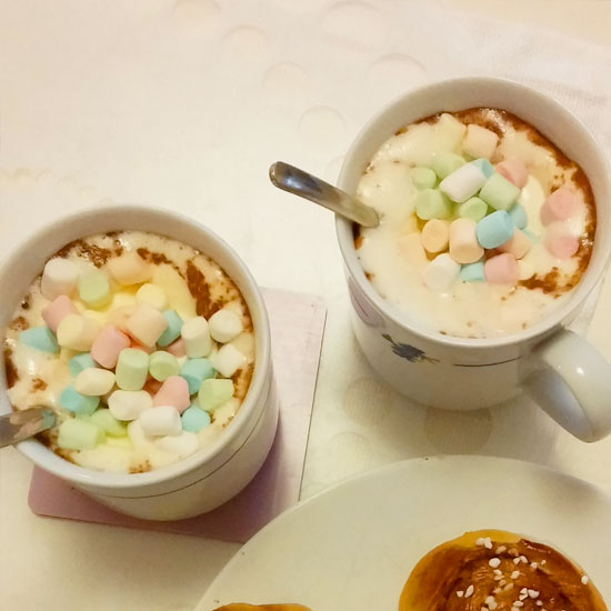 Kopp med varm choklad toppad med vispad grädde och minimarshmallows i olika pastellfärger